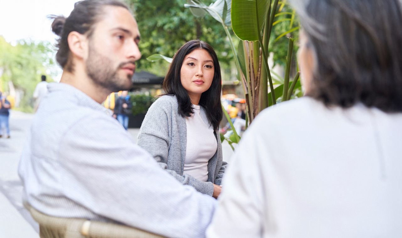 Three people sitting ouside by a busy street conversing 